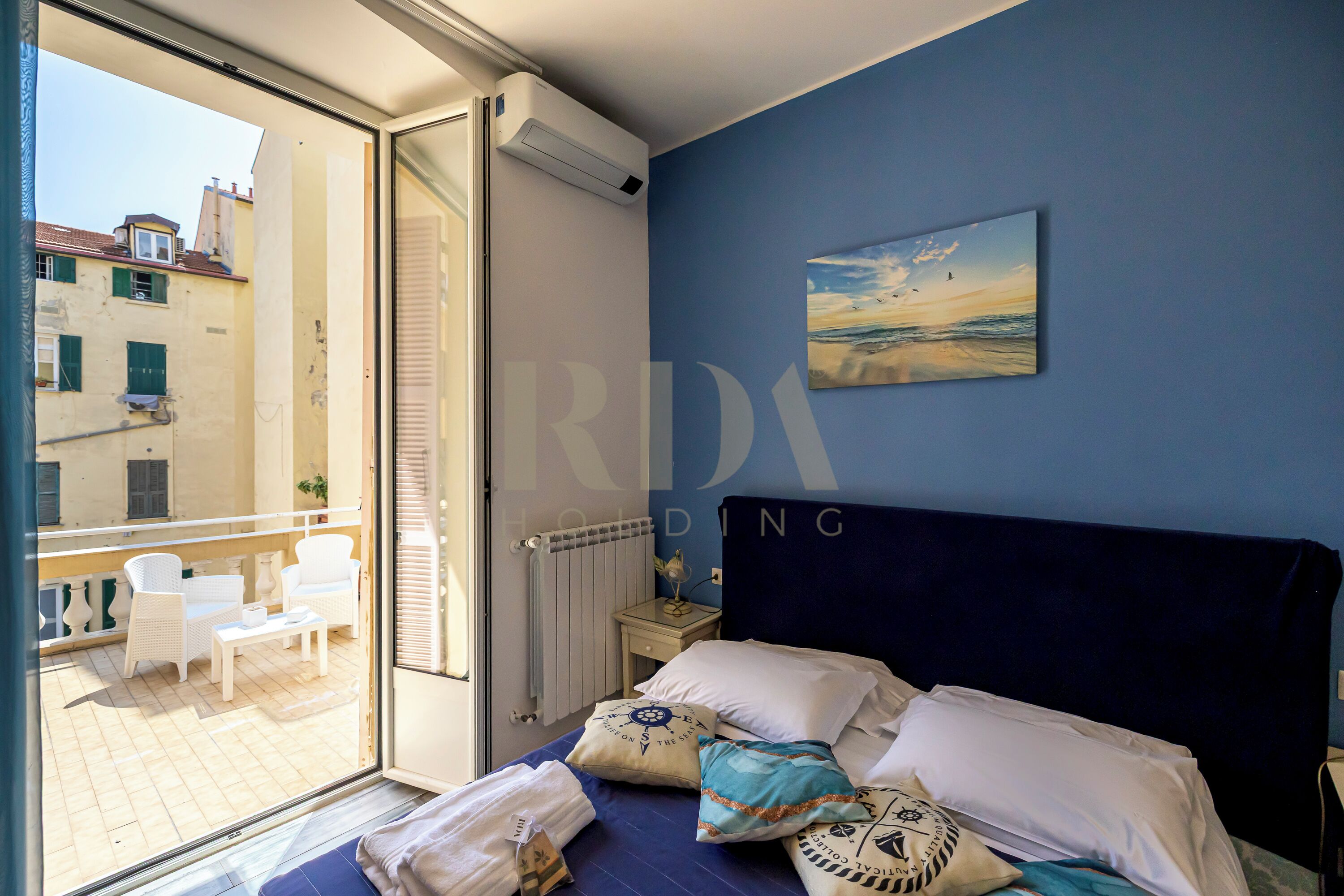 A bedroom with a bed, pillows, a nightstand, and a view of the outside balcony.