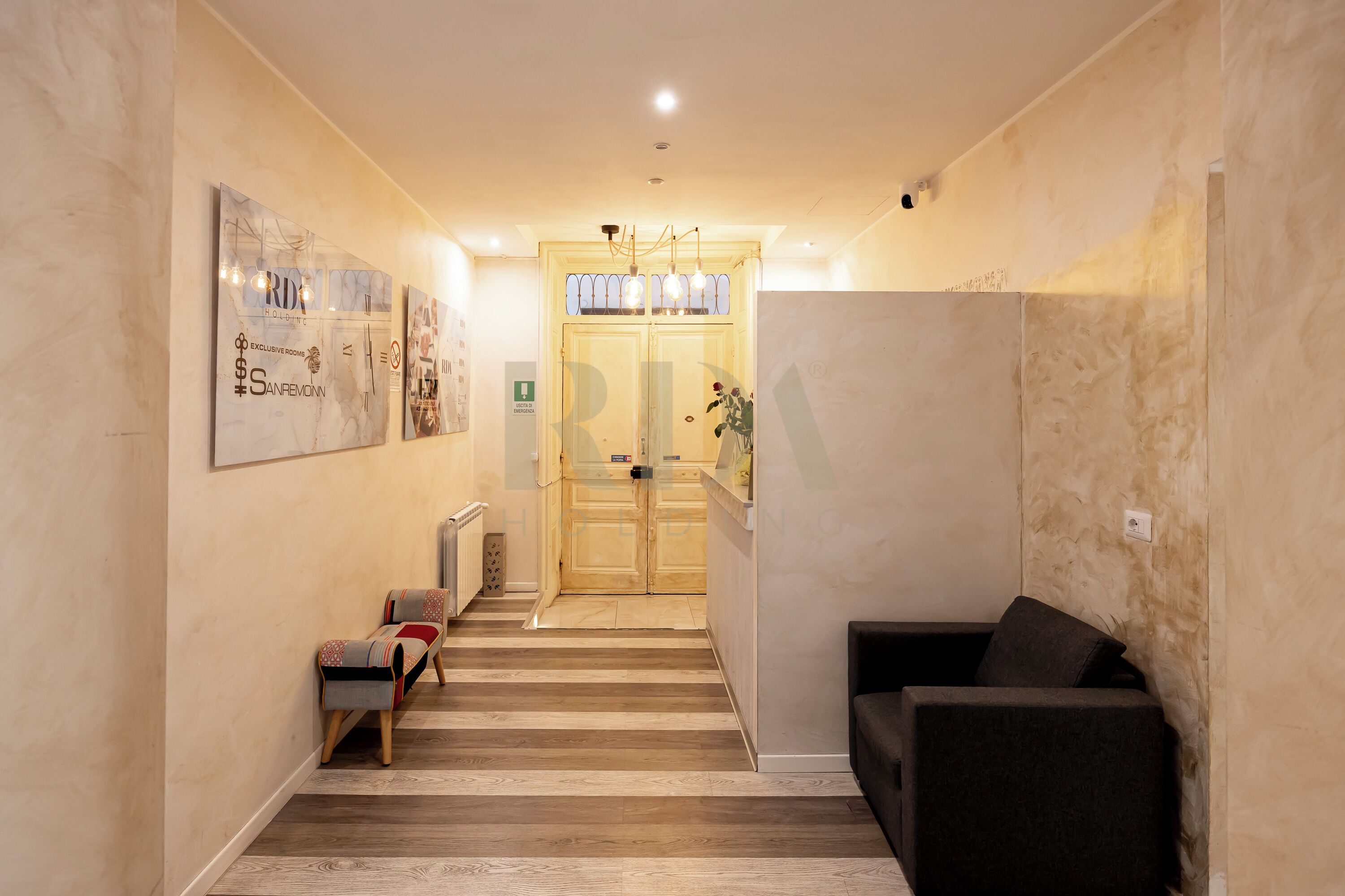 A hallway with a wooden floor, a bench, a sofa, and a door leading to a room.