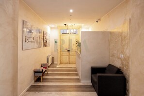 A hallway with a wooden floor, a bench, a sofa, and a door leading to a room. - SanremoInn Exclusive rooms (Sanremo)