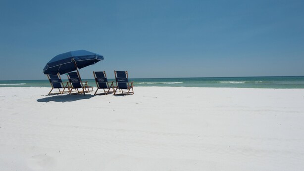 Une plage avec trois chaises longues placées sous un parasol bleu, face à l’océan.