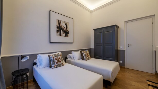 Une chambre d’hôtel avec deux lits, une armoire, un tableau encadré au mur et une petite table avec une lampe.