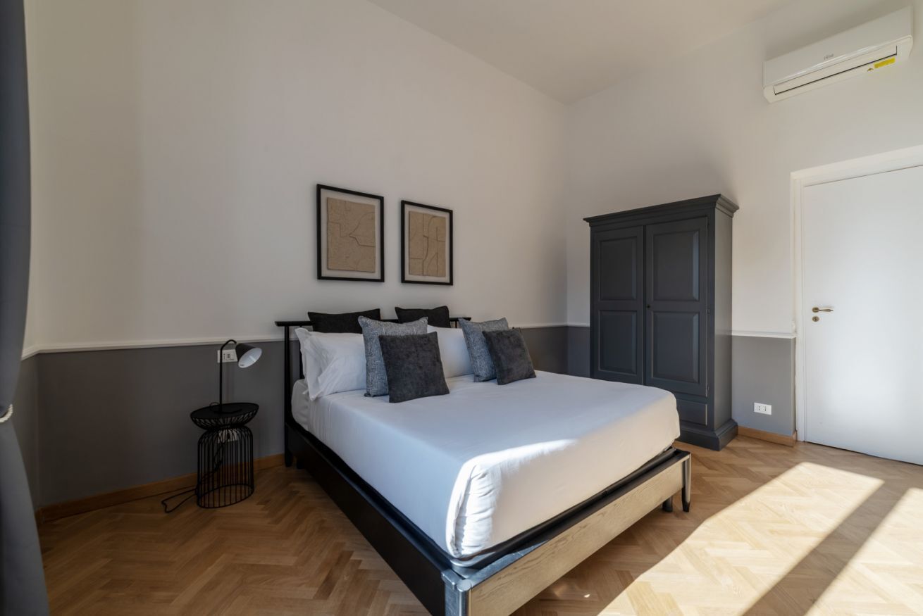 Una camera da letto con un letto, un armadio, una scrivania con una lampada e due quadri appesi al muro.