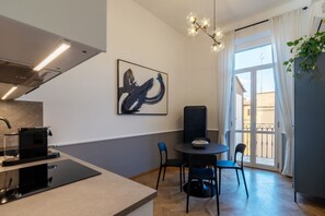 Eine moderne Küche mit Kaffeemaschine, ein Essbereich mit Tisch und Stühlen, ein großes abstraktes Gemälde und ein Balkon mit Vorhängen.