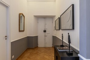 Ein Flur mit Holzboden, einer weißen Tür, einem Spiegel und zwei gerahmten Kunstwerken an der Wand.