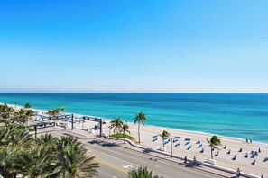 Une plage avec une route au premier plan, des palmiers et un ciel bleu dégagé.