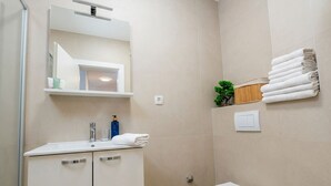 Een moderne badkamer met een wit wastafelmeubel, spiegel en toilet. Handdoeken en toiletartikelen liggen op het aanrecht.