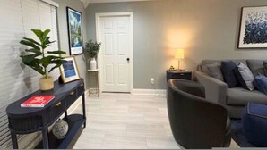 A living room with a grey sofa, a black armchair, a console table with a plant and a framed picture, and a door with a white frame. - Houston Home Near NRG Sleeps 6 (Houston)