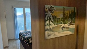 Une chambre à coucher avec un lit, un tableau représentant un paysage enneigé et une vue sur la mer depuis un balcon.