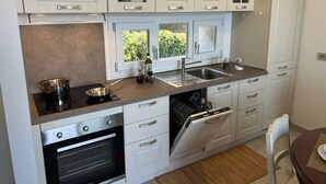 Une cuisine moderne avec des meubles blancs, un four encastré, un lave-vaisselle et une fenêtre donnant sur un espace verdoyant.