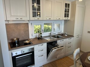 Une cuisine moderne avec des meubles blancs, un four encastré, un lave-vaisselle et une fenêtre donnant sur un espace verdoyant.