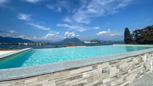 Une piscine bordée d’un mur en pierre, offrant une vue sur une ville lointaine et des montagnes.