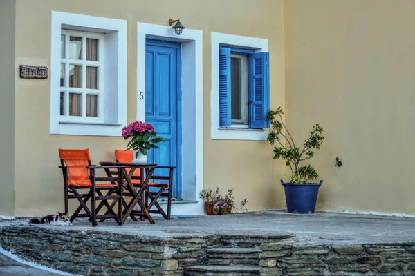 Exterior entrance with traditional blue door and seating area typical of Cycladic architecture.