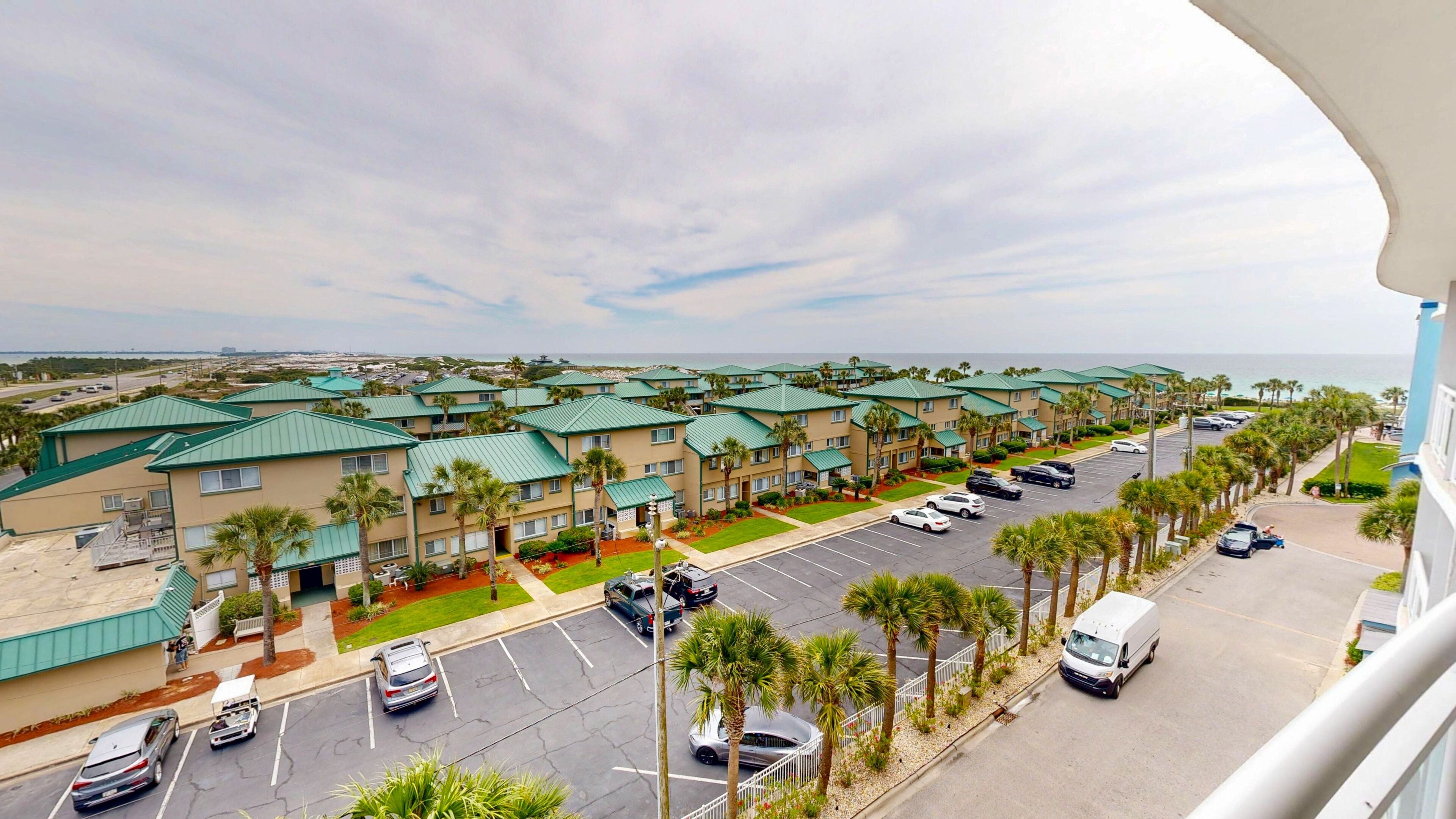 A hotel with multiple-story buildings, a parking lot, and a view of the ocean.
