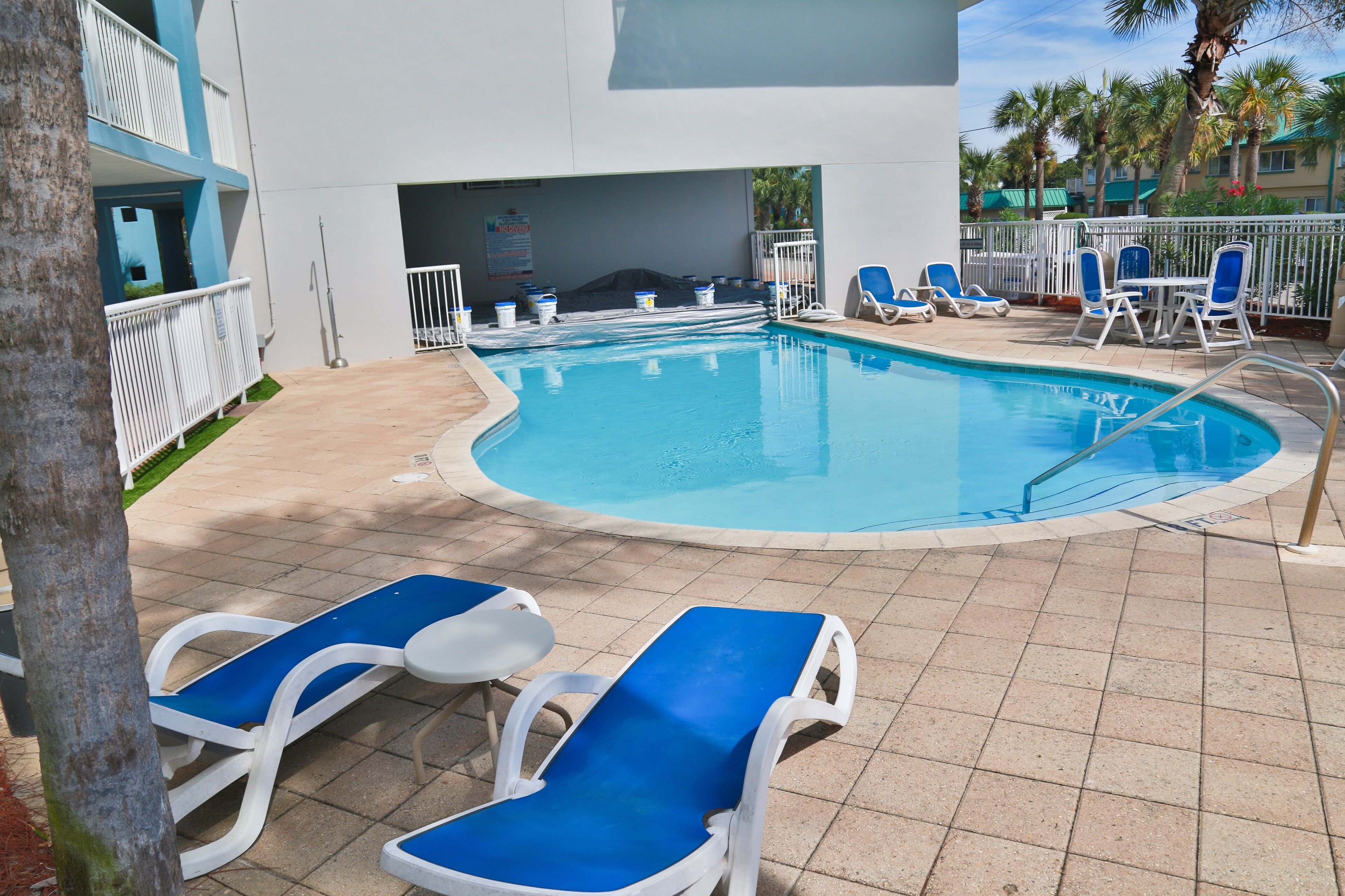 A pool area with blue and white lounge chairs, a pool, and a building with a white exterior and blue accents.