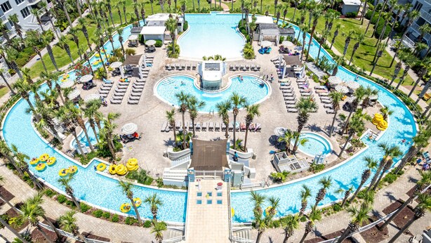 A large, circular swimming pool with multiple lanes, surrounded by palm trees and sun loungers. - Destin West Gulfside V509 Condo (Fort Walton Beach)