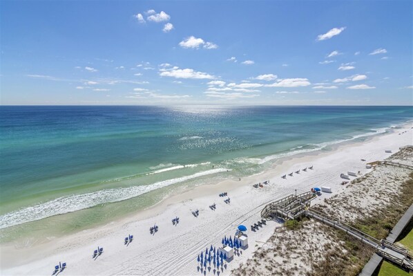 A beach with a clear sky, calm sea, and a sandy shore with umbrellas and beach chairs. - Shoreline Towers 1111 3 Bedroom Condo (Destin)