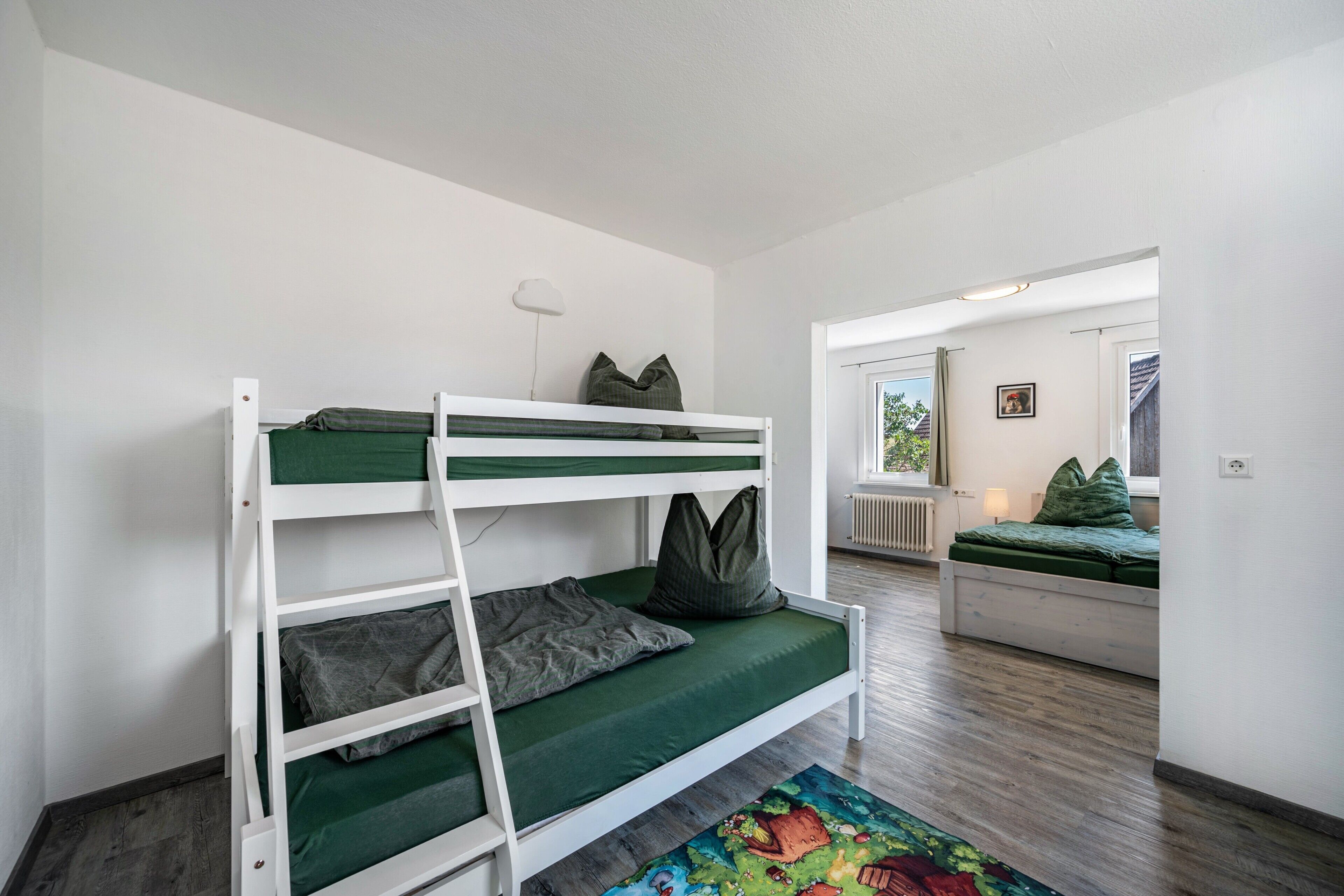 A bunk bed with green bedding, a ladder, and pillows. There is a window with a view of the outdoors.
