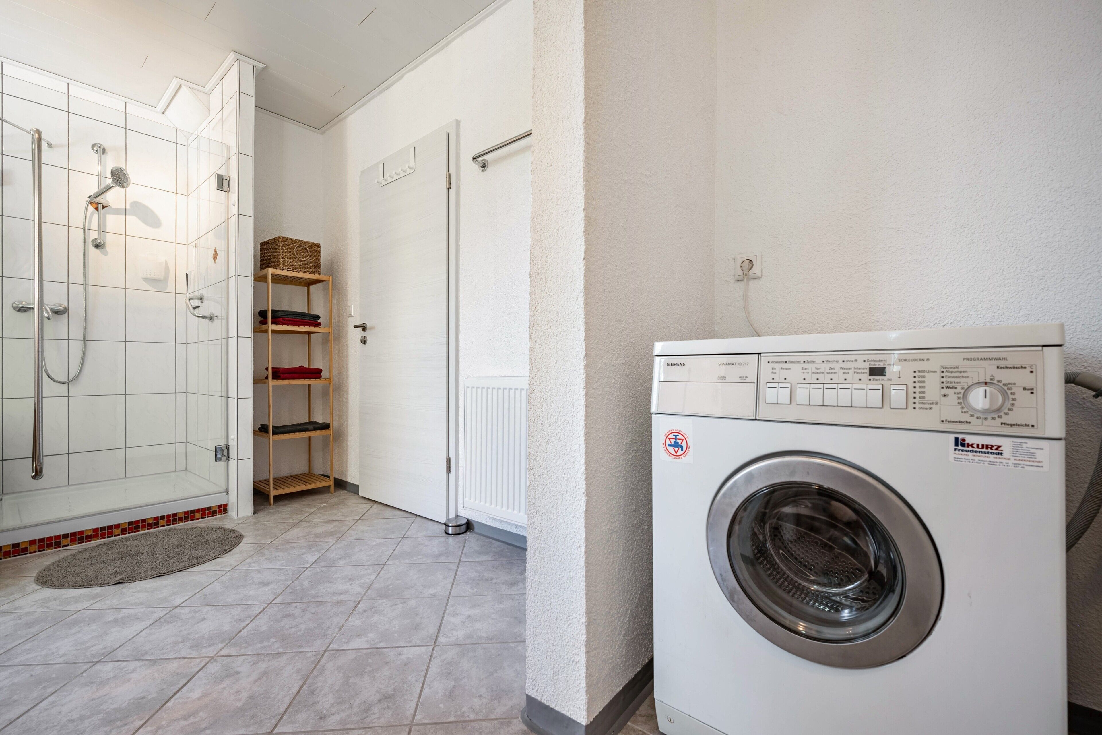 A laundry room with a washing machine, a shower, and a shelf with folded towels.