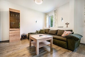 Ein Wohnzimmer mit Holzboden, einem grünen Sofa, einem Couchtisch aus Holz, einem Schrank und einem Fenster mit Vorhängen.