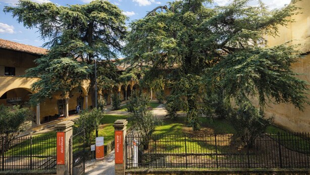 A courtyard with a pathway, trees, and a building with arches. - Vista Lumina by MMega (Florence)