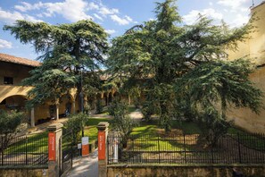 A courtyard with a pathway, trees, and a building with arches. - Vista Lumina by MMega (Florence)