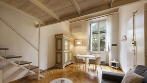 A spacious room with a wooden staircase, a dining area with a white table and chairs, a gray sofa, and a window with a view of greenery. - Vista Lumina by MMega (Florence)