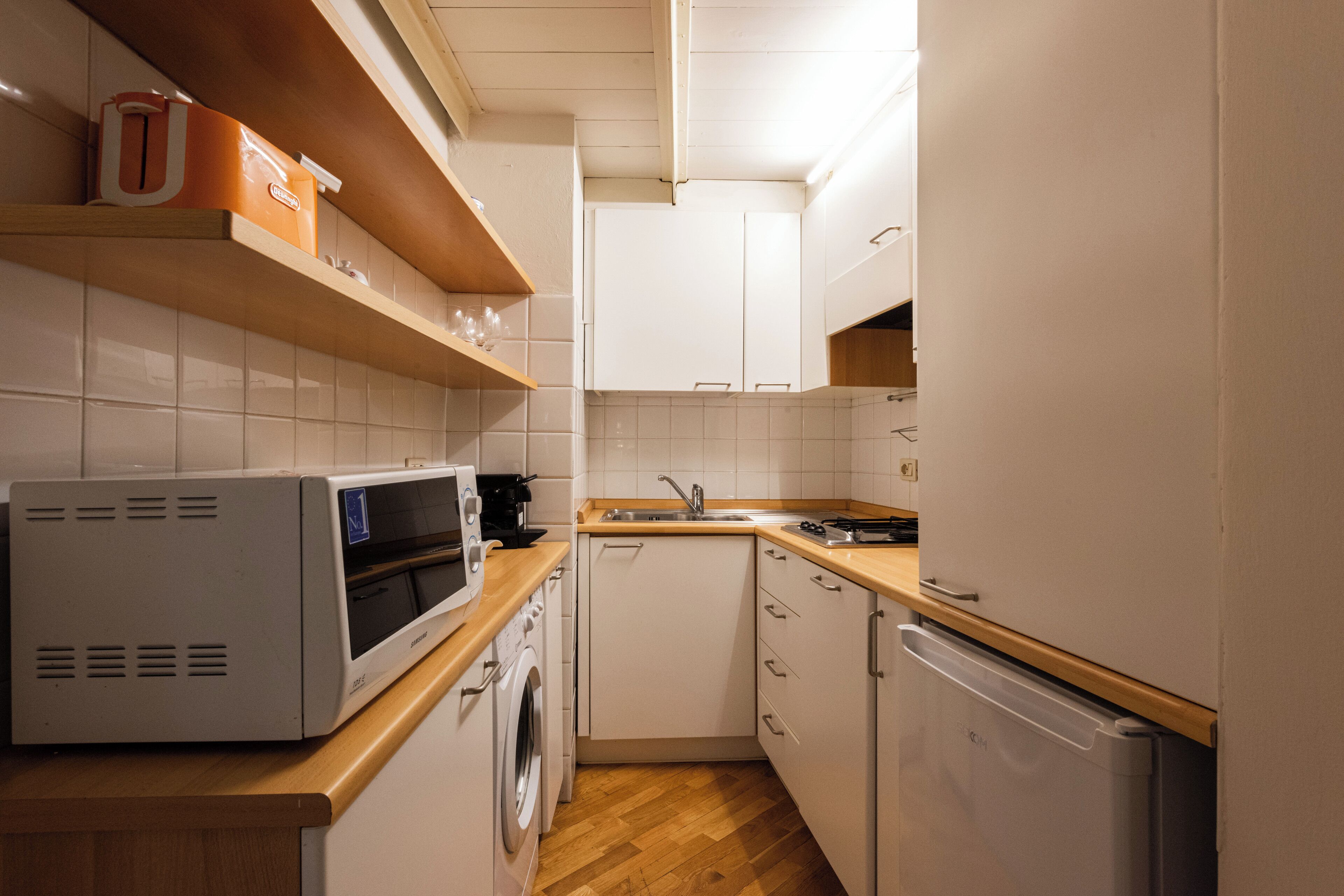 A compact kitchen with white cabinets, a microwave, a washing machine, and a refrigerator.