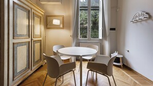 A dining area with a round table and four chairs, a radiator, a window with curtains, and a cabinet with decorative moldings. - Vista Lumina by MMega (Florence)