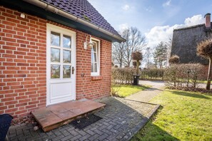 A brick house with a white door, a small porch, and a garden with grass and shrubs. - Apartment 'Niemark Gestüt Kriseby' with Shared Terrace and Wi-Fi (Lübeck)