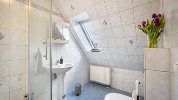 Ein Badezimmer mit Duschkabine aus Glas, einem Standwaschbecken, einer Toilette und einem Heizkörper.