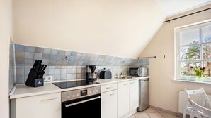 Une cuisine avec des meubles blancs, un fourneau noir, un four à micro-ondes et une fenêtre donnant sur les arbres.