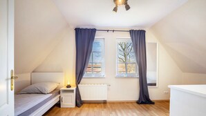 Une chambre à coucher comprenant un lit, une table de chevet, une fenêtre avec des rideaux, un radiateur et un ventilateur de plafond.