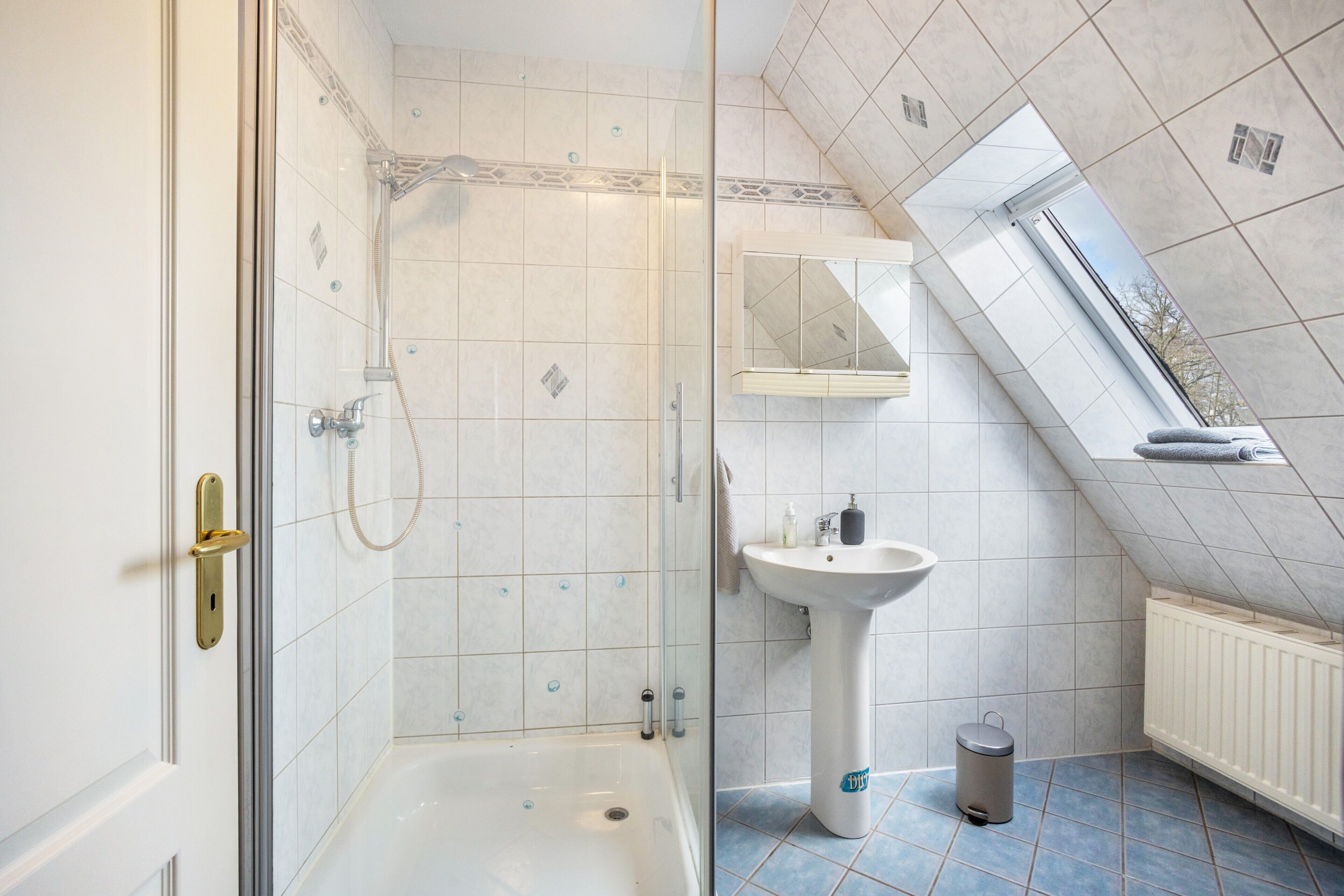 Un bagno con doccia, lavandino, specchio e finestra.
