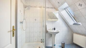 Un bagno con doccia, lavandino, specchio e finestra.