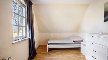 A small, single-bed room with a window, a radiator, and a white dresser.
