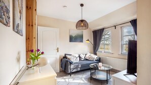 Un salon moderne avec un canapé, une table basse ronde, un téléviseur, une suspension et des œuvres d’art accrochées aux murs.