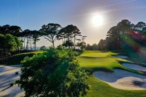 Ein Golfplatz mit Sandbunkern, Bäumen und blauem Himmel.