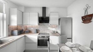 Una cocina moderna con armarios blancos, horno integrado, microondas y un letrero con la palabra 'café' en la pared.