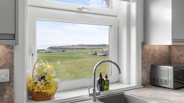 Una cocina con vista a un campo cubierto de hierba y coches aparcados.