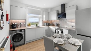 Una cocina moderna con lavadora incorporada, un comedor con mesa dispuesta para cuatro personas y vistas al exterior a través de una ventana.