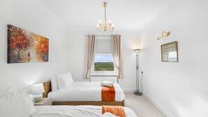 Un dormitorio con cama, un cuadro, una araña, una lámpara de pie y una ventana con vistas.
