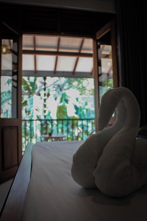 Un lit agrémenté d’une serviette en forme de cygne, avec vue sur un balcon verdoyant.