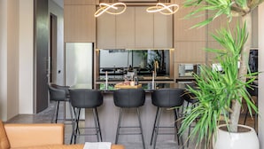 A modern kitchen with a bar area, black bar stools, and a potted plant. - Pera Villa Ubud Bali. (Ubud)