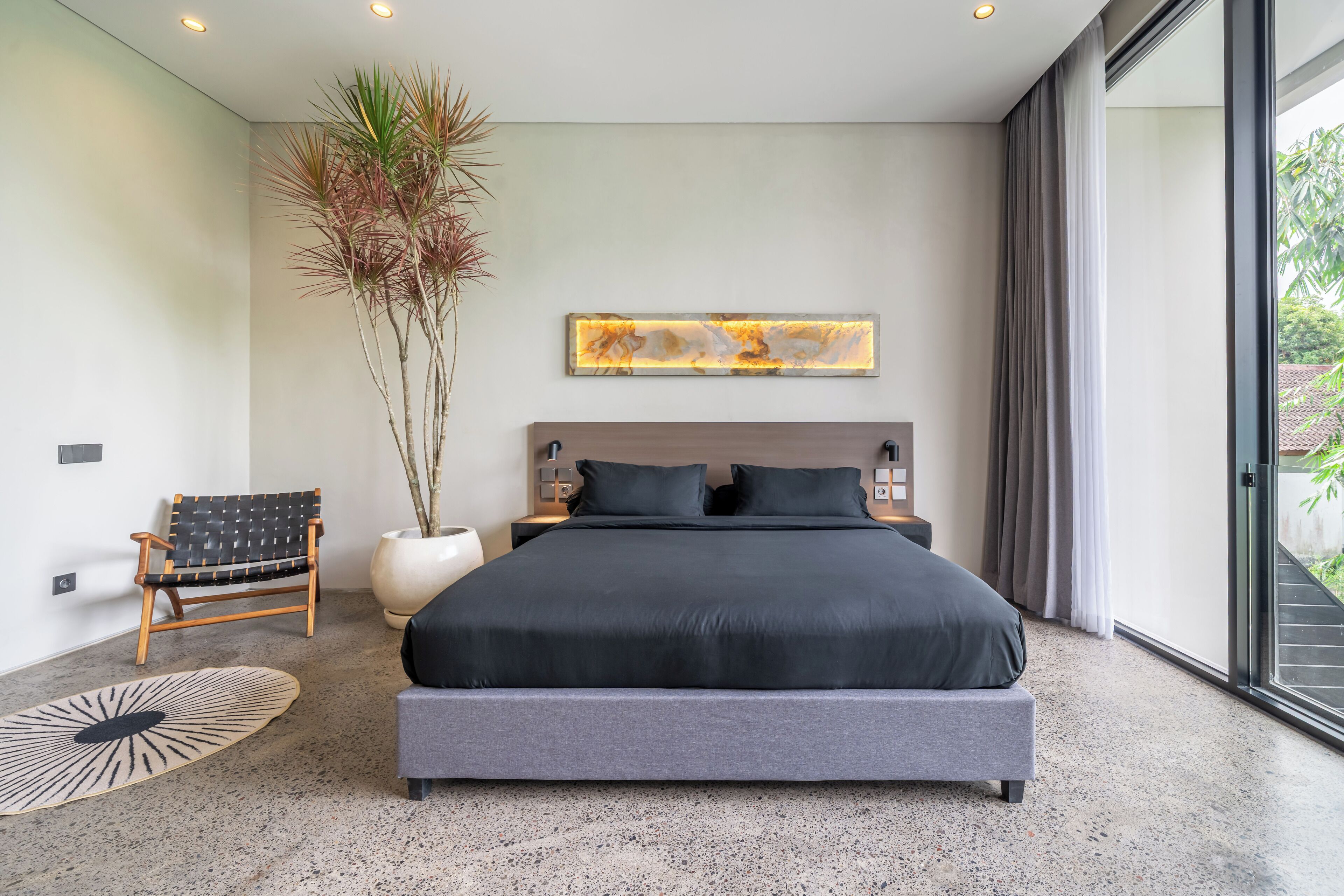 Une chambre à coucher moderne avec un grand lit, une chaise, une plante en pot et un luminaire fixé au mur.