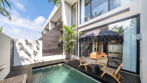 A modern outdoor pool area with wooden deck, lounge chairs, and a large umbrella. - Pera Villa Ubud Bali. (Ubud)
