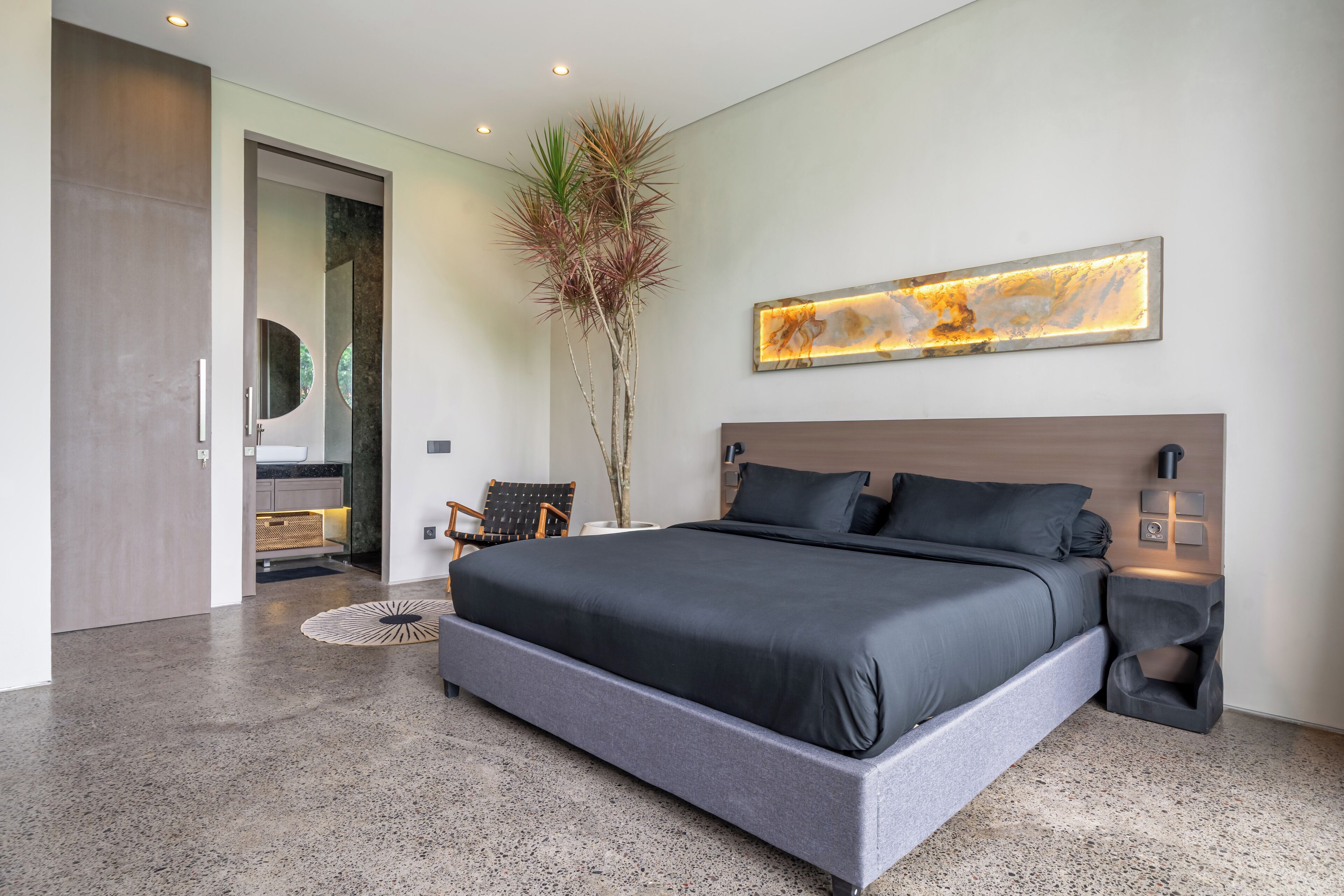 Una camera da letto moderna con un letto grande, un comodino, una lampada a parete e una pianta decorativa.