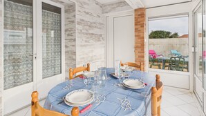 A dining area with a table set for four, a brick column, and a view of the outside. - House for 5 with garden, beach 500m away (Saint-Hilaire-de-Riez)