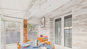 A dining area with a table set for four, a wooden chair, a clock, and a door with patterned glass panels. - House for 5 with garden, beach 500m away (Saint-Hilaire-de-Riez)