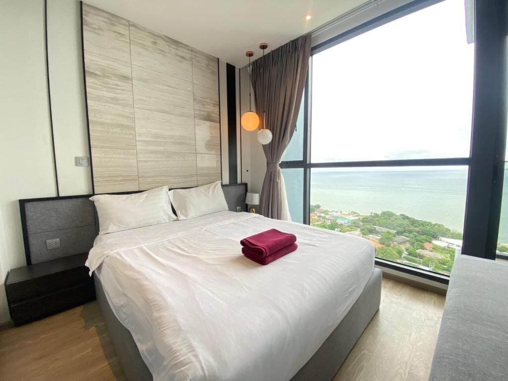 Una camera d'albergo moderna con un letto grande, un comodino, una lampada e vista sul mare.