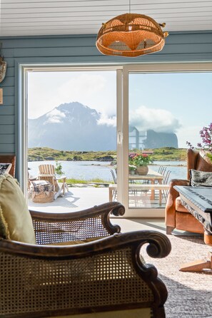 A room with a large sliding glass door leading to a deck with outdoor seating and a view of a mountain.